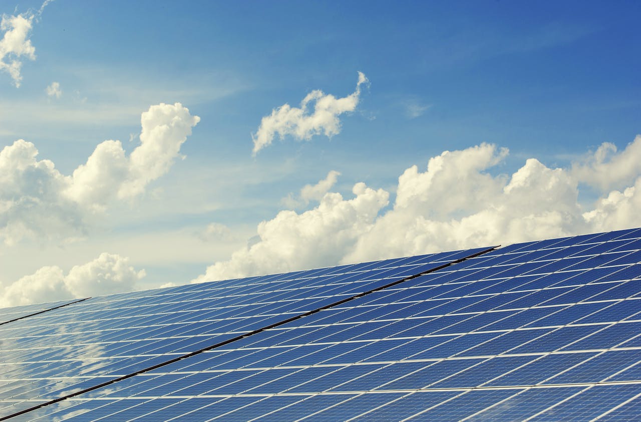 Services Sleek modern solar panels under a vibrant blue sky with clouds, symbolizing clean energy.